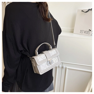 Detail of grey crossbody bag featuring geometric texture and silver turn-lock clasp