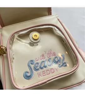 Detail of cream backpack with pink trim and transparent pocket with elegant embroidery