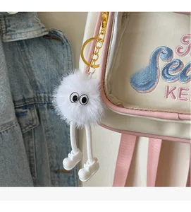 Close-up of a cute white plush monster keychain with big eyes and gold metal clip on a bag