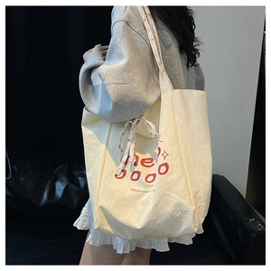 Détail du sac cabas en toile avec lettrage rouge et ruban floral rose porté par mannequin
