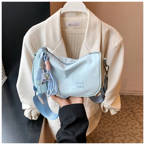Detail of light blue pleated shoulder bag with wide strap and lemon charm accessory