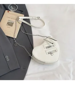 Detail of white heart-shaped crossbody bag with gold zippers and chain strap on soft white background