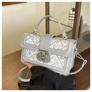 Close-up of geometric embroidered pattern and matte silver twist lock on leather bag