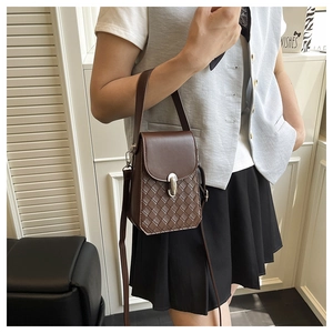 Detail of dark brown crossbody bag with woven texture, metal clasp and leather strap
