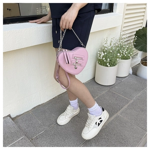 Detail of pink heart-shaped bag featuring dual zippers and silver heart-shaped charms