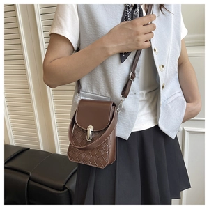 Close-up of a woven dark brown crossbody bag with a silver metal clasp on a model