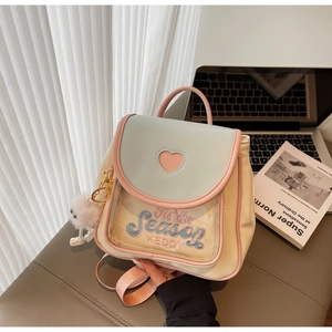 Detail of a mini cream and blue backpack with heart applique and plush ball charm
