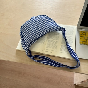 Detailed close-up of blue gingham canvas crossbody bag on a book with striped strap
