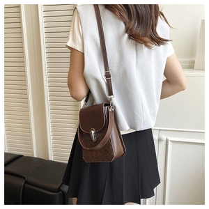 Detail of dark brown leather crossbody bag featuring woven texture and metal lock