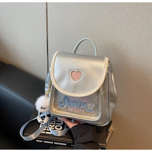 Detail of silver mini backpack featuring pink heart cutout and white pompom charm