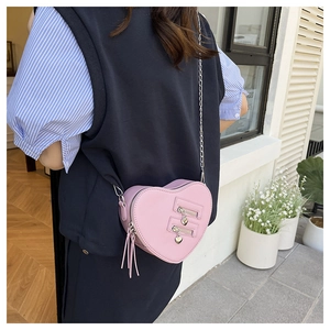 Pink heart-shaped crossbody bag detail with twin zippers, heart charms and tassels