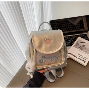 Close-up of silver backpack with pink heart cutout, floral embroidery and plush charm