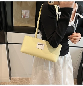 Detail of light yellow patent leather shoulder bag with embroidered brand logo label