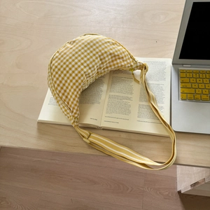 Detailed top view of a yellow gingham half-moon canvas bag on a book and laptop