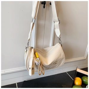 Detail of off-white crescent bag featuring wide woven strap and yellow charm ornament