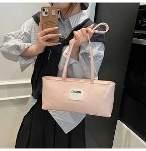 Detail of light pink patent leather shoulder bag with white fabric logo tag and slim strap