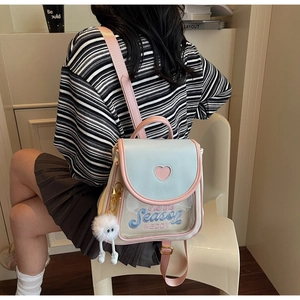 Detail of blue and white mini backpack featuring heart cutout and plush ball pendant