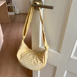 Detail of a yellow gingham crescent bag with adjustable wide strap hanging on a white door