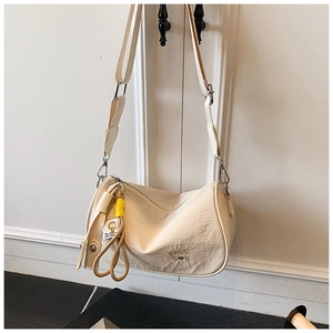 Close-up of cream textured fabric cylinder bag with wide strap and yellow charm detail