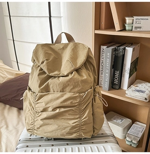 Détail d'un sac à dos en nylon kaki avec poches plissées sur une valise blanche