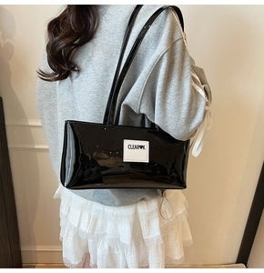Detail showing high-gloss black patent leather shoulder bag with white logo patch