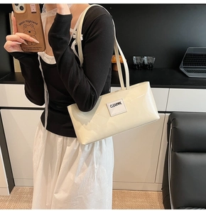 Detail of white patent leather underarm bag featuring a glossy finish and logo lettering