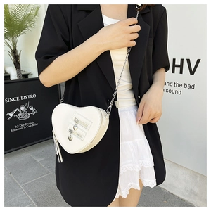 Detailed close-up of white heart-shaped crossbody bag with decorative tassels and silver chain