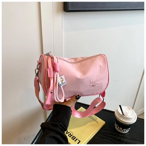 Pink nylon boston bag with embroidered letters and a wide strap held in a hand