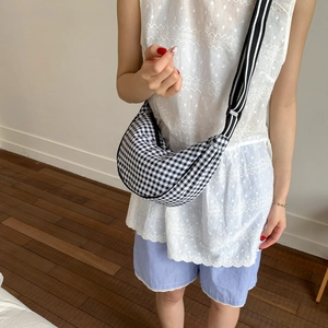 Detail of checkered crescent bag featuring a black and white striped wide strap
