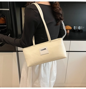 Detail of minimalist cream faux leather shoulder bag featuring a stitched heart logo patch