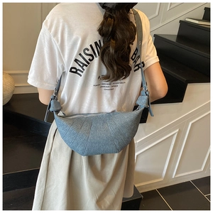 Detail view of the denim blue crescent crossbody bag with pleated texture on the model