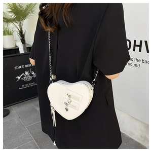 Close-up of white heart-shaped crossbody bag with gold chain strap and tassel detail