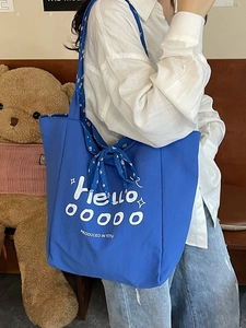 Blue canvas tote bag with white Hello print and floral ribbon bow in casual style