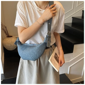 Detail view of denim crescent bag with metallic eyelets on wide strap worn by model