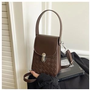 Detailed view of dark brown woven leather bag with silver capsule buckle on a book