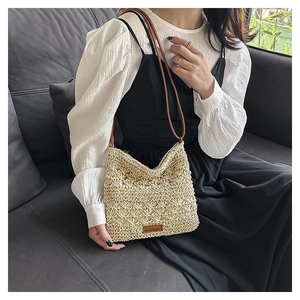 Detail of hand-woven hollow straw bag with brown leather label and slim shoulder strap