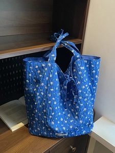 Quilted blue floral canvas tote bag with ribbon tie closure on a rustic wooden desk