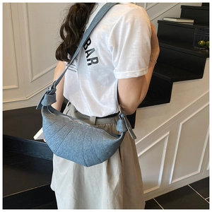 Detail of light blue denim crescent bag with curved stitching and knot strap detail