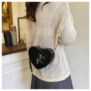 Close-up of heart-shaped black crossbody bag with silver chain on model in cafe setting