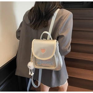 Detail of light blue glossy mini backpack with heart embroidery and plush ball charm
