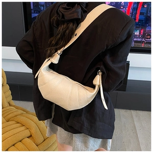 Model view of cream croissant crossbody bag with quilted texture and wide shoulder strap