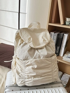 Sac à dos minimaliste beige en nylon avec cordon de serrage posé sur une valise blanche