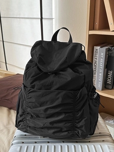 Sac à dos noir en nylon plissé avec cordons sur une valise blanche dans une chambre