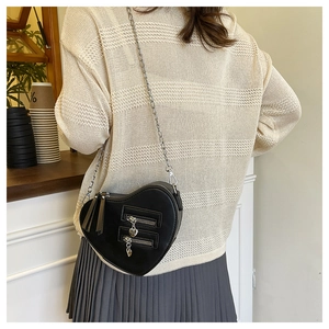 Detail of a black heart-shaped crossbody bag with metal zippers and chain strap on model