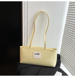 Detail of light yellow patent leather underarm bag with a white fabric logo tag