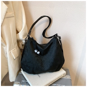 Detail of floral embossed black tote bag with white bead charm on silver suitcase