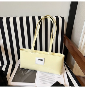 Detail view of cream yellow patent leather tote bag with CLEAR K logo on striped background