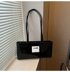 Close-up of black glossy patent leather shoulder bag with CLEAR K logo on white label