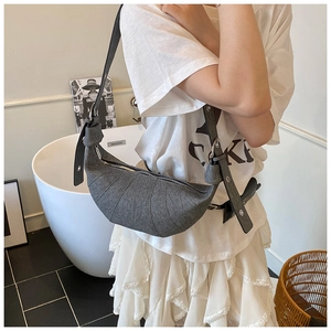 Close-up of a dark grey tweed croissant bag with curved stitching and knotted strap details