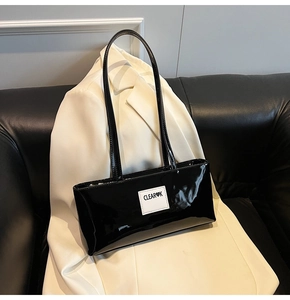 Detail of a black glossy leather baguette bag featuring a white square Clear K logo tag
